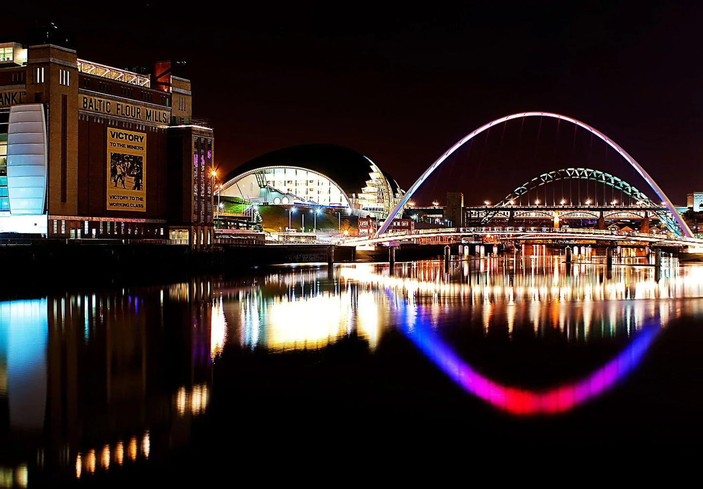 Newcastle Quayside at night with the Gateshead Millennium Bridge and Tyne Bridge illuminated over the River Tyne.