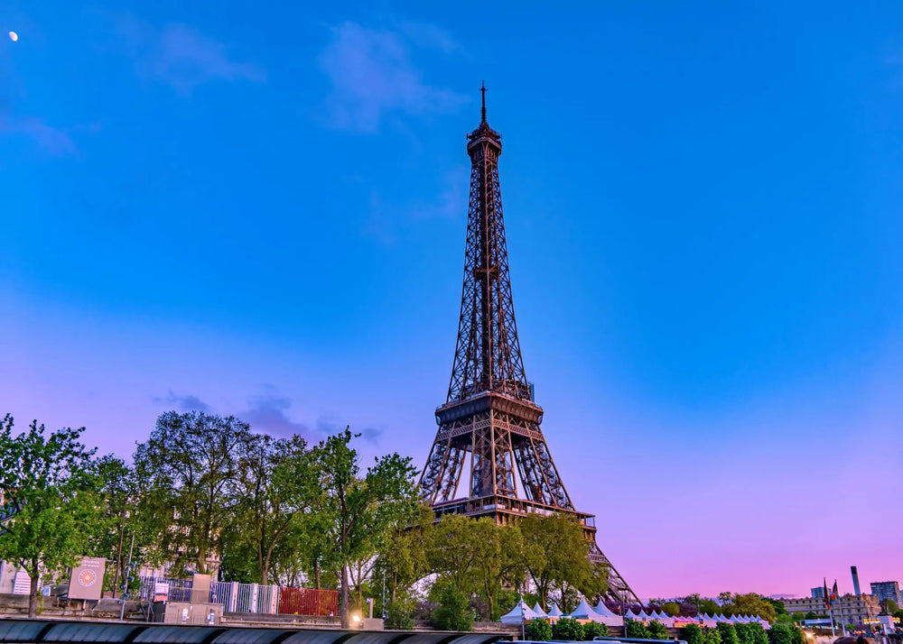 Eiffel Tower rising above trees beneath a blue and pink evening sky in Paris