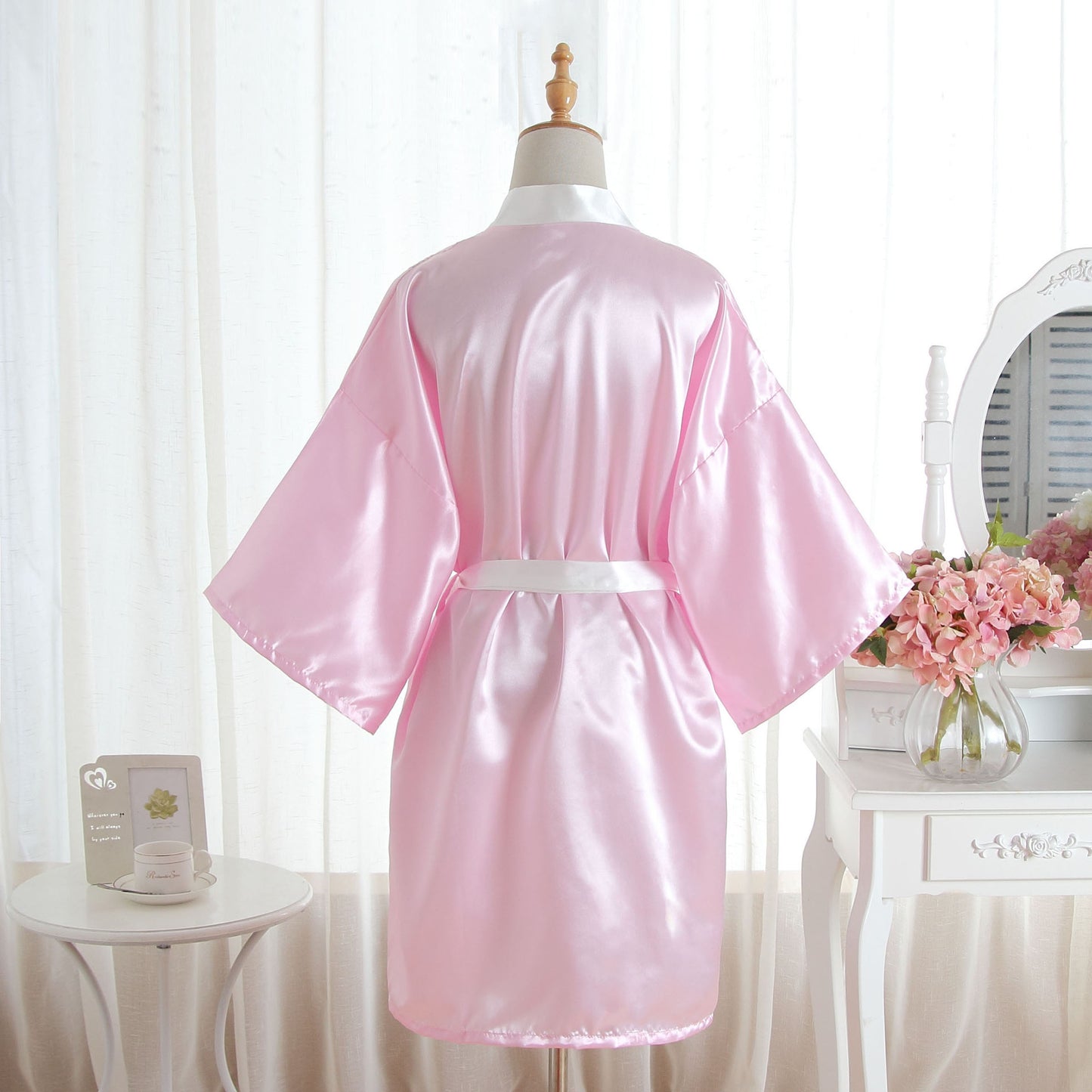 A light pink satin robe displayed on a mannequin torso, shown from the back. The robe has wide sleeves and a matching waist tie.