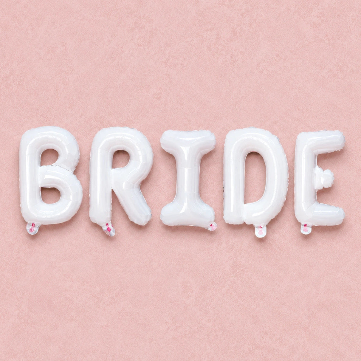 White foil letter balloons spelling out the word 'BRIDE' arranged in a row on a textured light pink background.