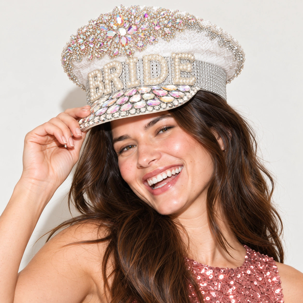 A smiling bride-to-be wearing a white bridal-style hat covered in rhinestones and crystals, with the word "BRIDE" spelled out across the front. 
