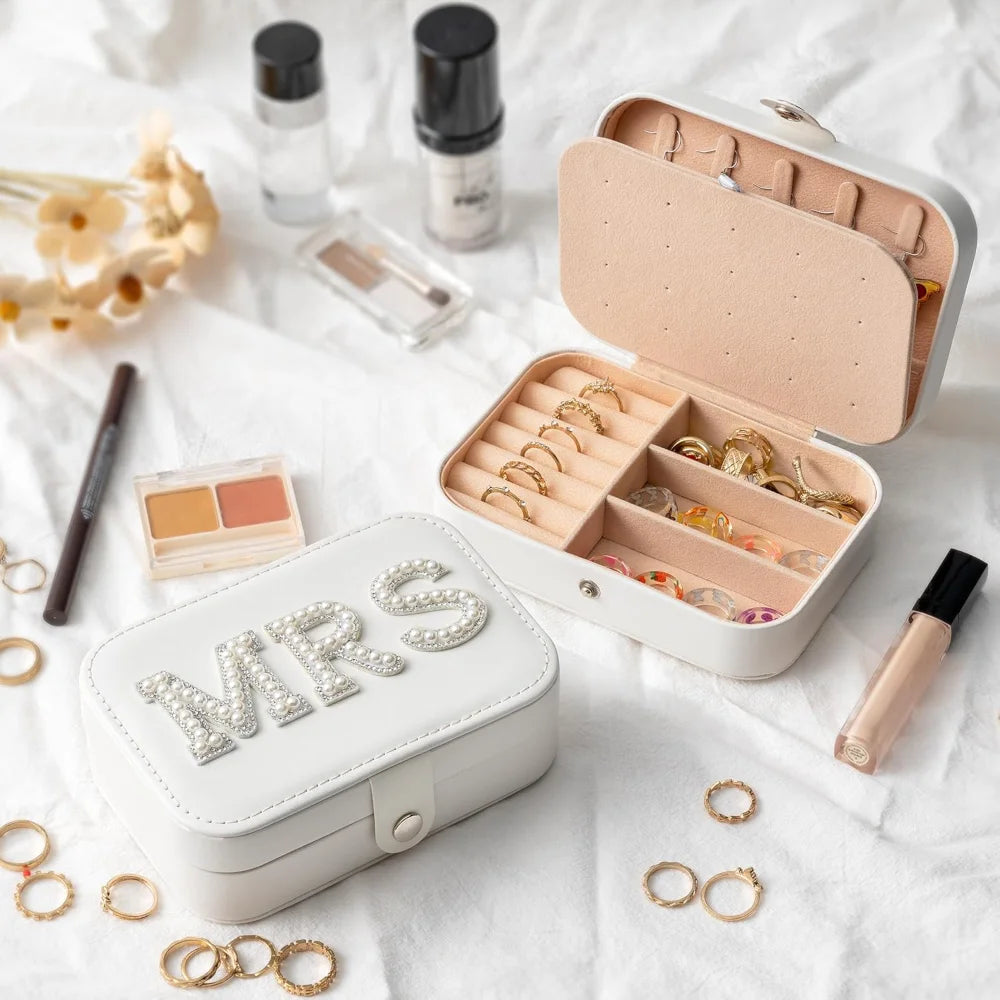 Jewelry case with 'MRS' on a white surface with makeup items.