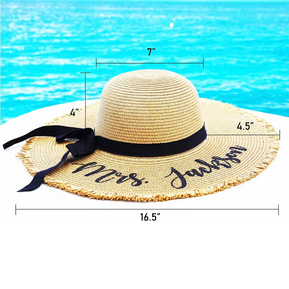 Beige straw hat with black ribbon and 'Mrs. Jackson' text, measurements shown, against a blue water background.