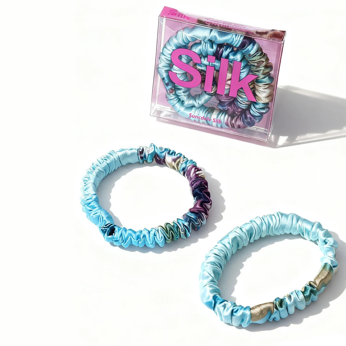 Set of colorful blue scrunchies with a 'Silk' branded box on a white background