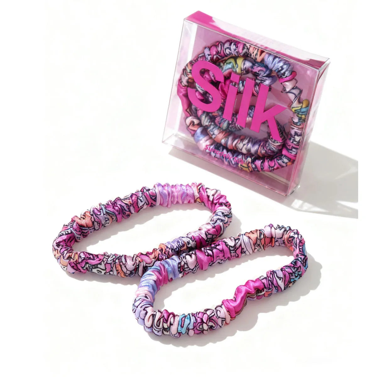 Colorful hair ties with a pink 'Silk' box on a white background