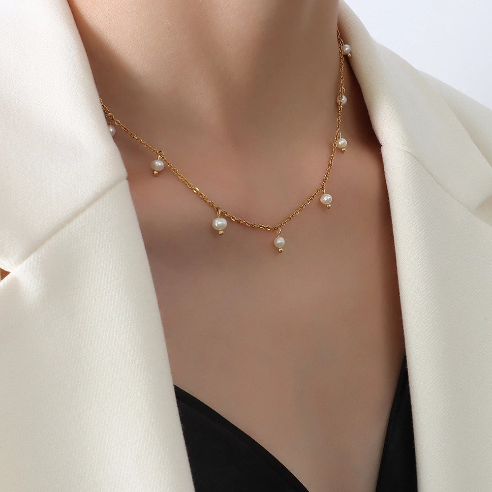 Gold necklace with pearls worn by a person in a white blazer