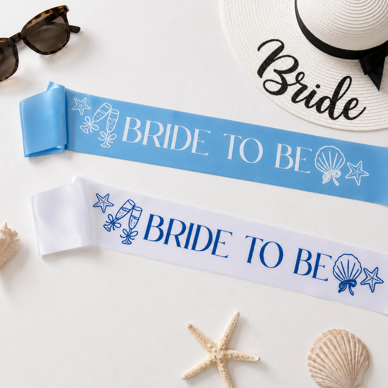 Two 'Bride to Be' sashes on a white surface with beach-themed accessories.