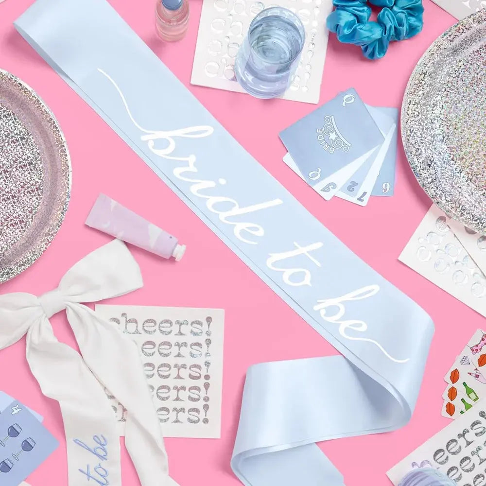 Bride to be sash on a pink background with party supplies