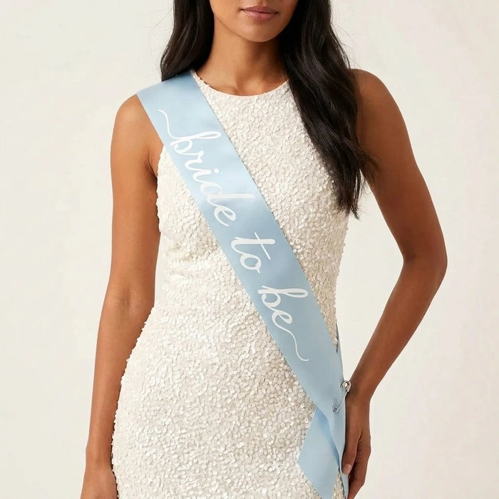 Woman wearing a white dress with a blue sash that says 'bride to be' on a plain background