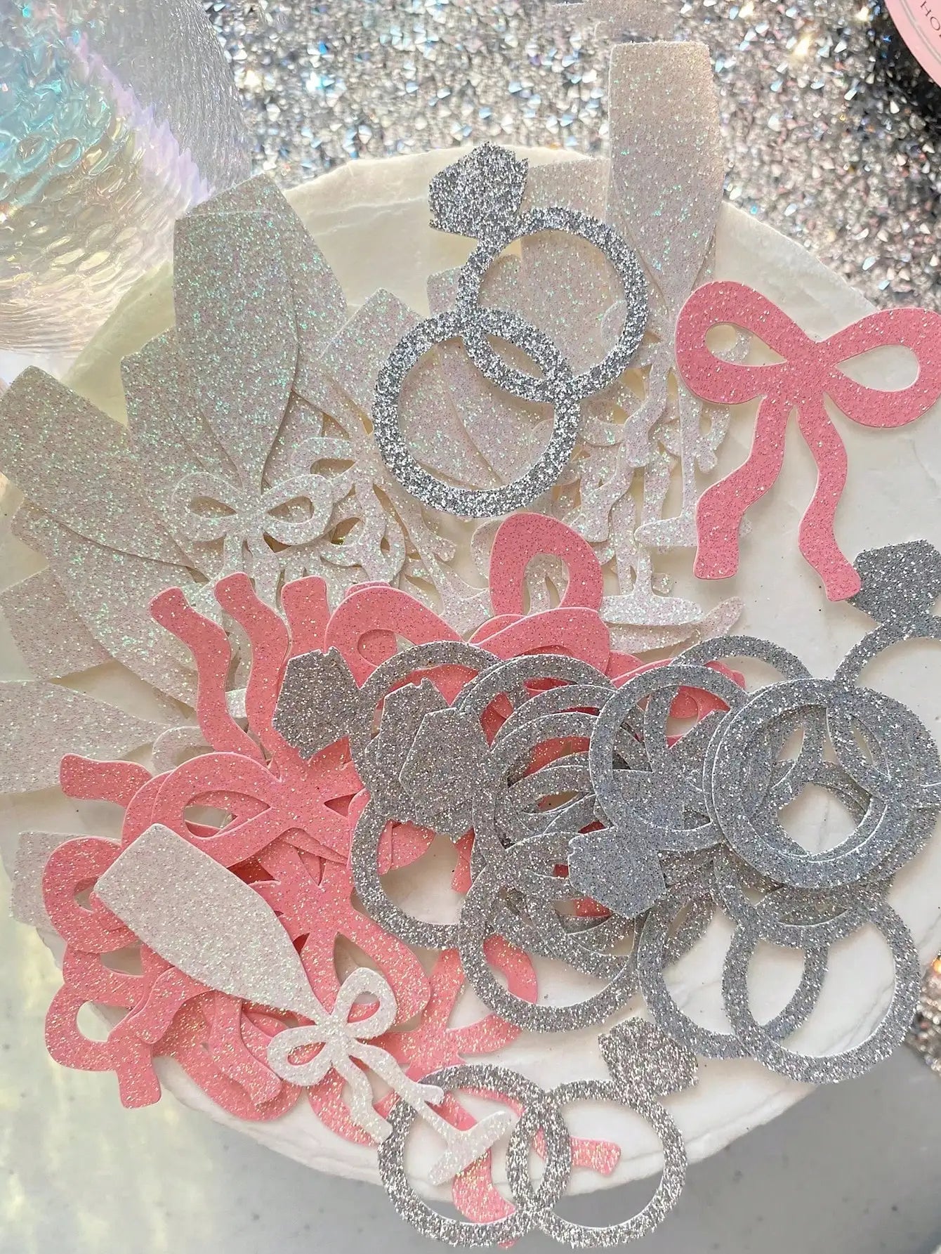 Decorative confetti with pink and silver designs on a glittery background