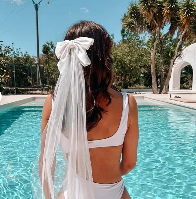 Bride -to-be wearing a white bow veil while sitting in a pool.