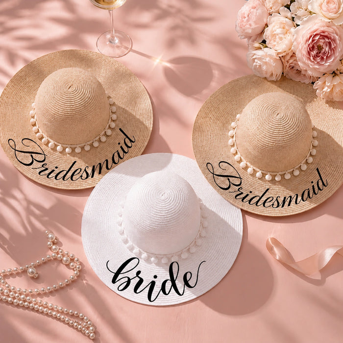 Bride and bridesmaid personalized wide-brim sun hats arranged on a soft pink backdrop with blush flowers, champagne, pearls, and ribbon, featuring two natural straw hats labeled "Bridesmaid" and one white hat labeled "Bride."