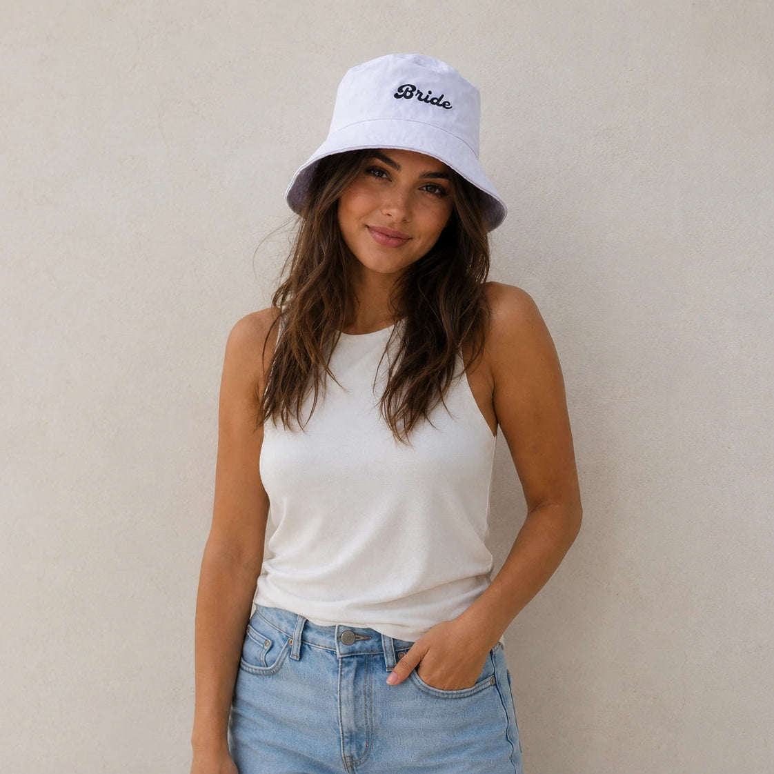 Woman wearing a white 'Bride' bucket hat against a plain background