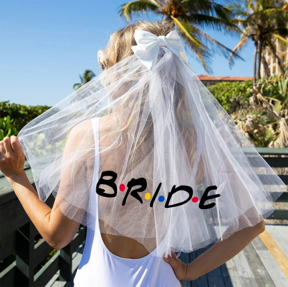 Person wearing a white veil with a large bow, standing outdoors with palm trees in the background.