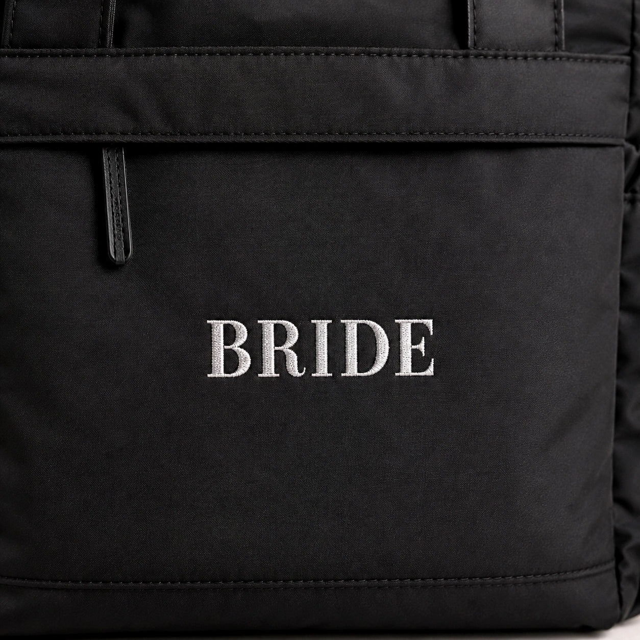 Close-up of a black fabric bag or backpack with the word "BRIDE" embroidered in white serif letters on the front.