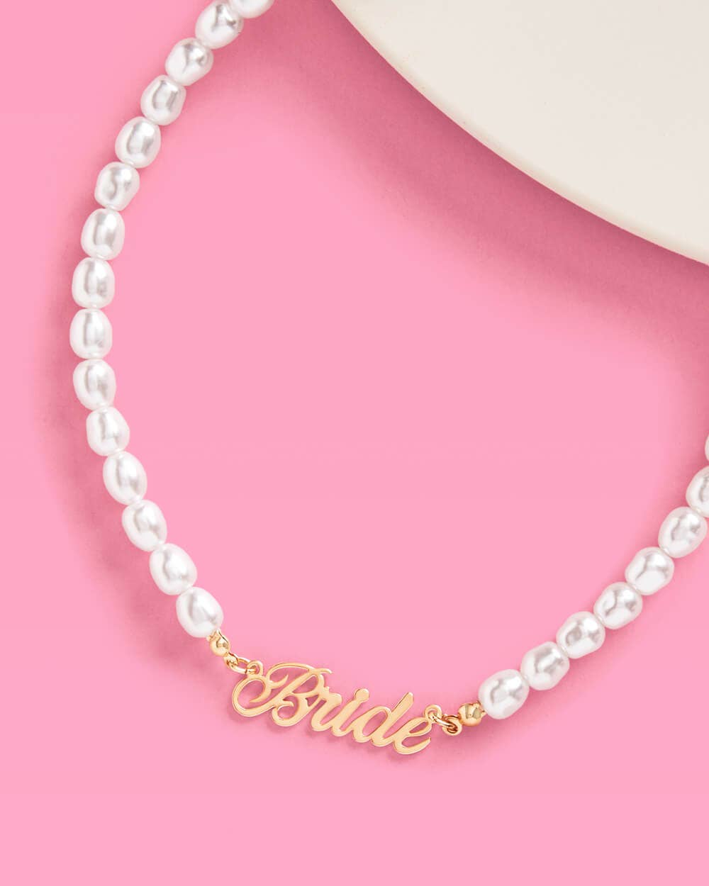 Bride pearl necklace with faux pearls and gold bride nameplate on pink background