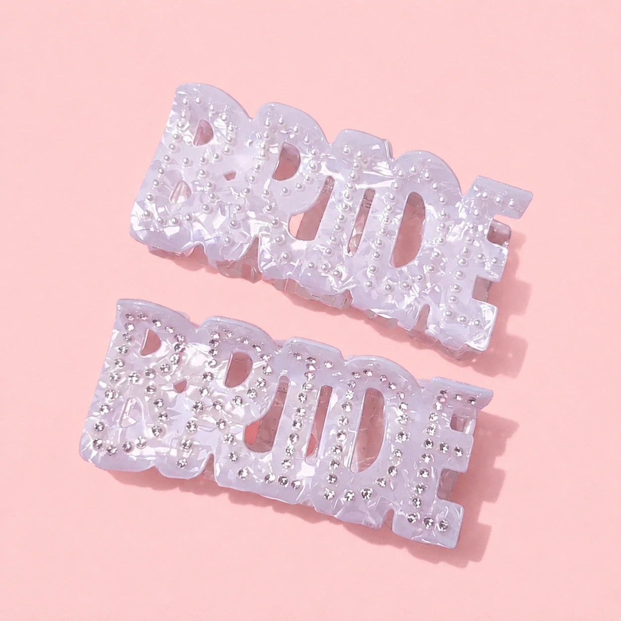 Two 'Bride' hair clips with rhinestones on a pink background