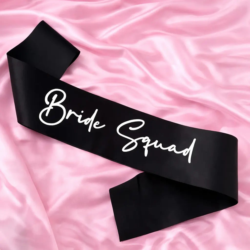 Black sash with 'Bride Squad' text on a pink fabric background