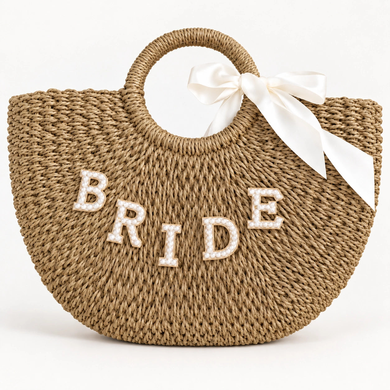Natural tan bride straw tote bag with circular handles, pearl-effect lettering and an ivory bow on a plain background.