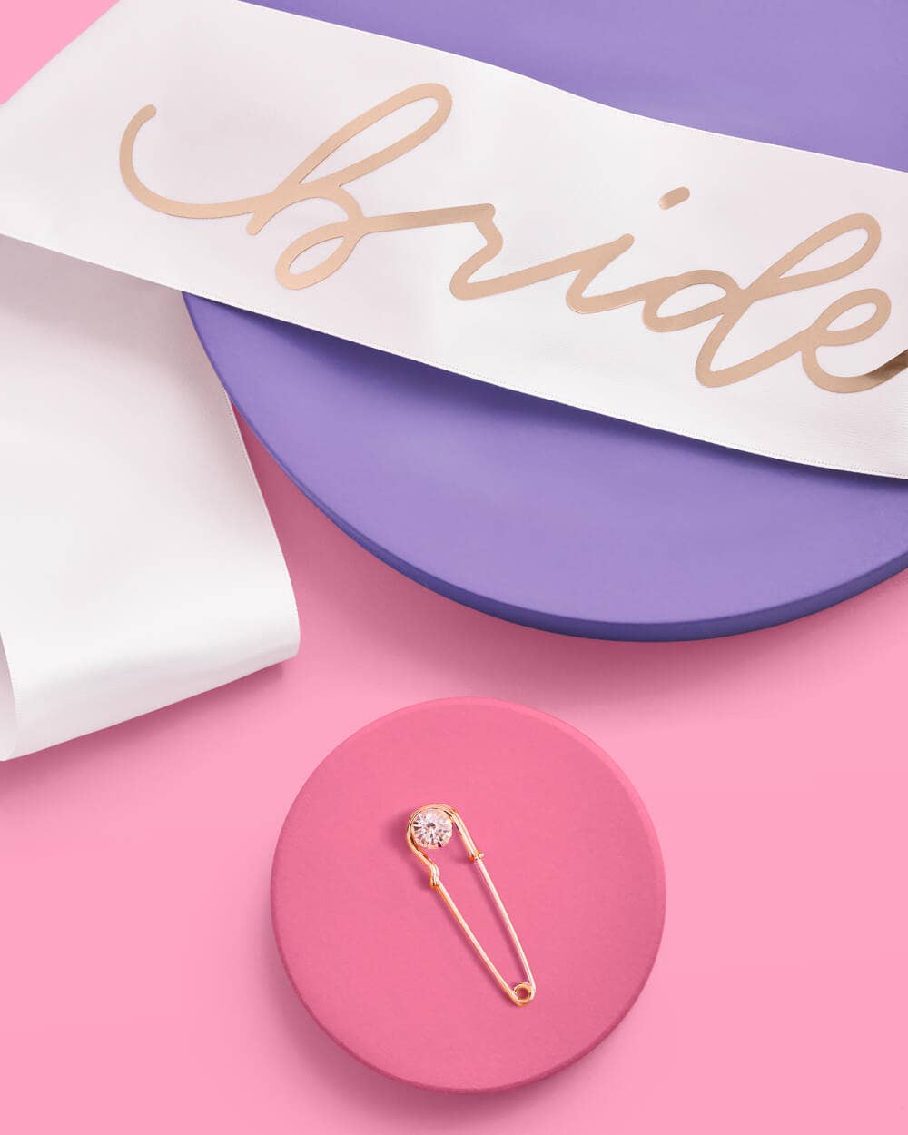 White sash with 'Bride' text on a purple and pink background with a gold brooch.