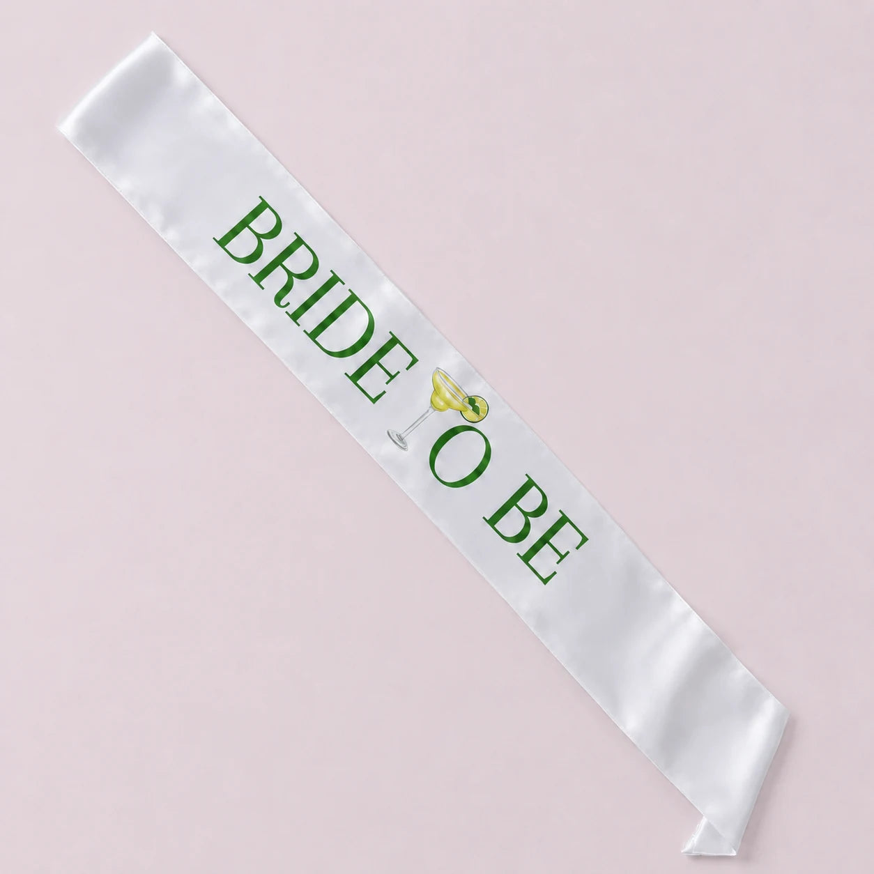 White sash with 'BRIDE TO BE' text and a green teardrop design on a light pink background