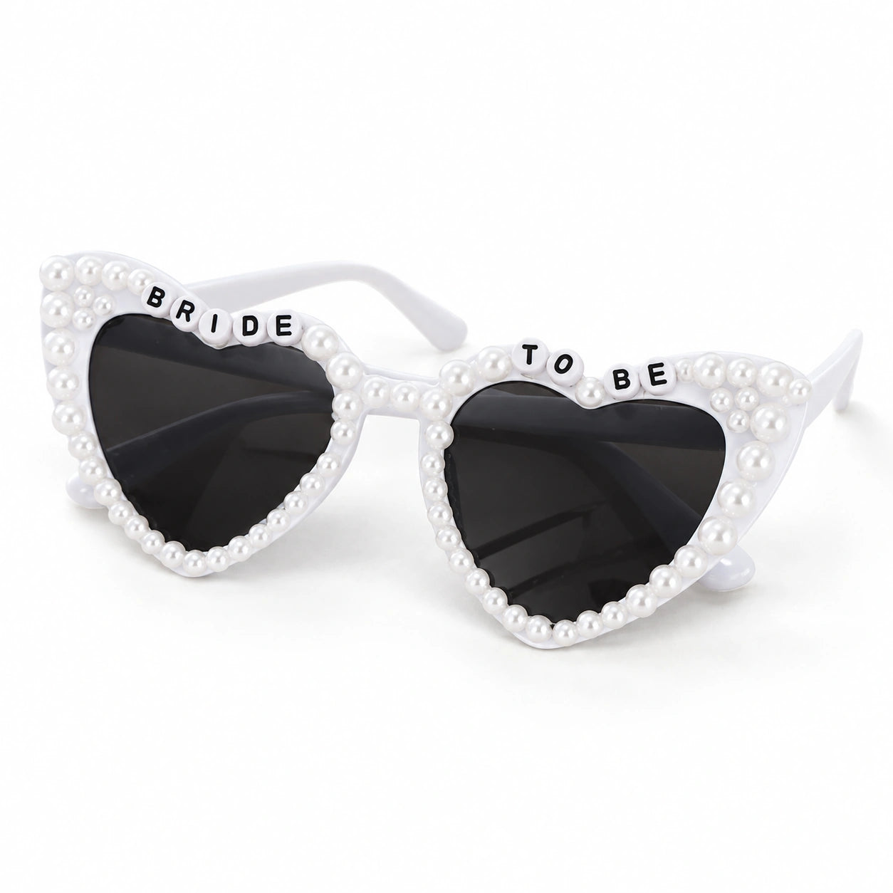 White heart-shaped sunglasses with pearl embellishments around the frames and the words 'BRIDE TO BE' printed on the top of each lens, set against a plain white background.