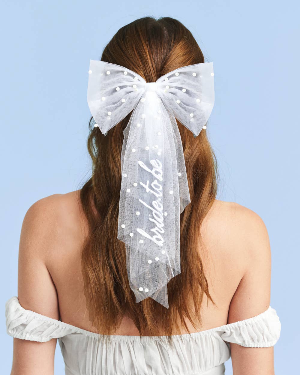 Back view of bride wearing white pearl hair bow with embroidered bride to be detail