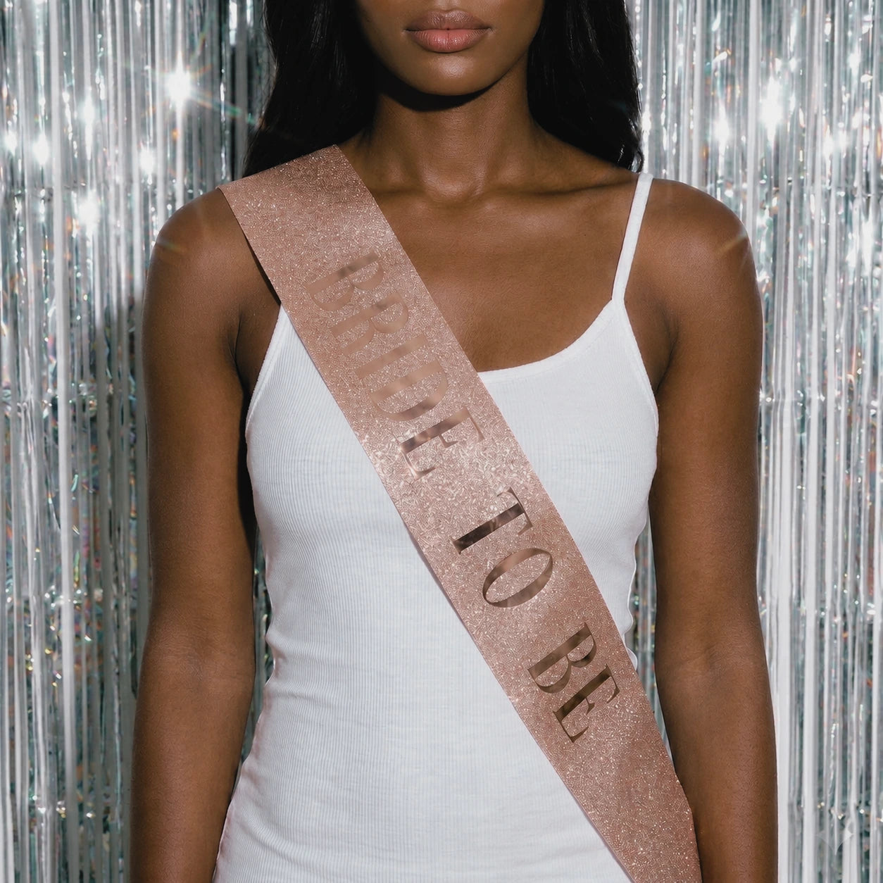 Woman wearing a 'Bride To Be' sash against a silver tinsel background
