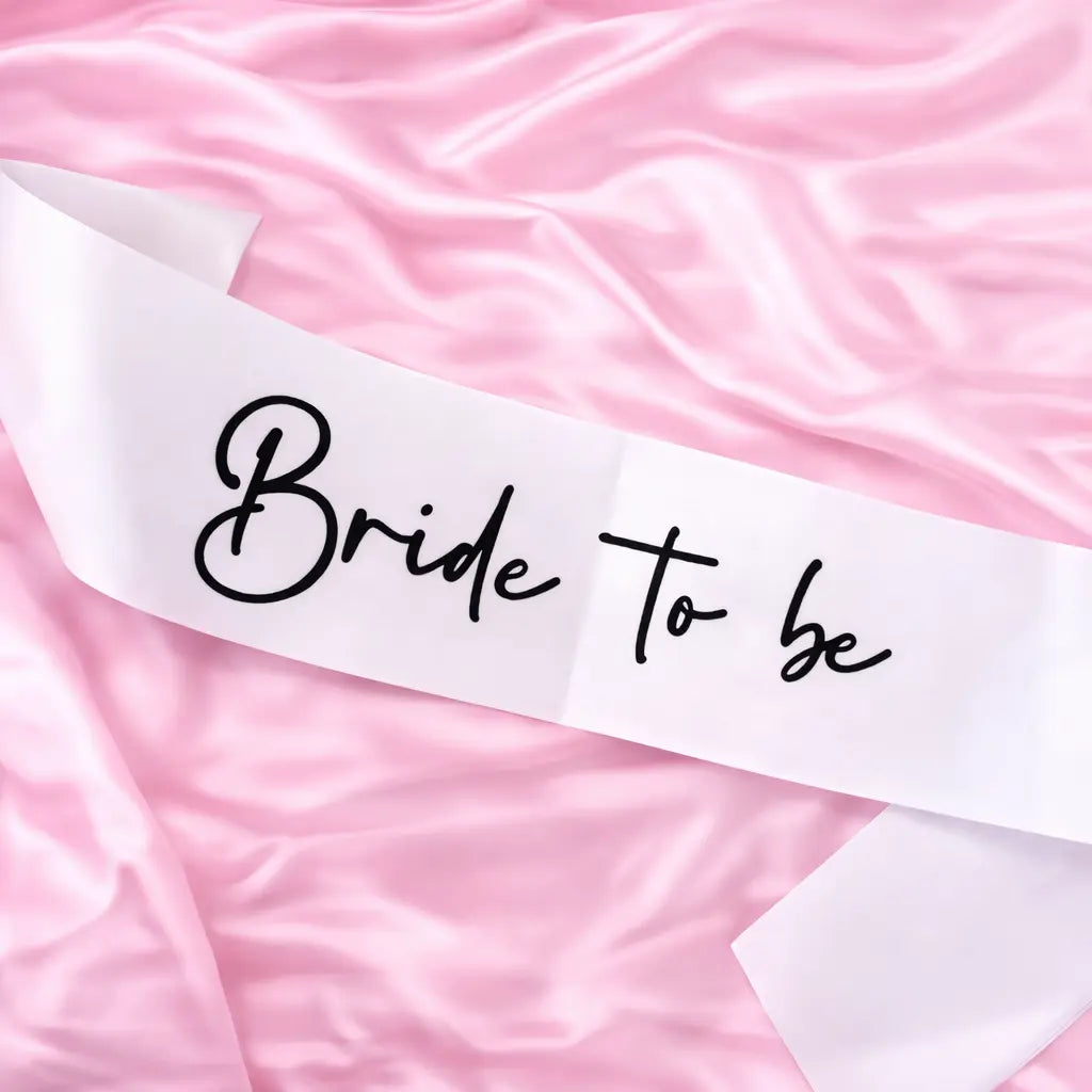 White sash with 'Bride To Be' text on a pink satin background