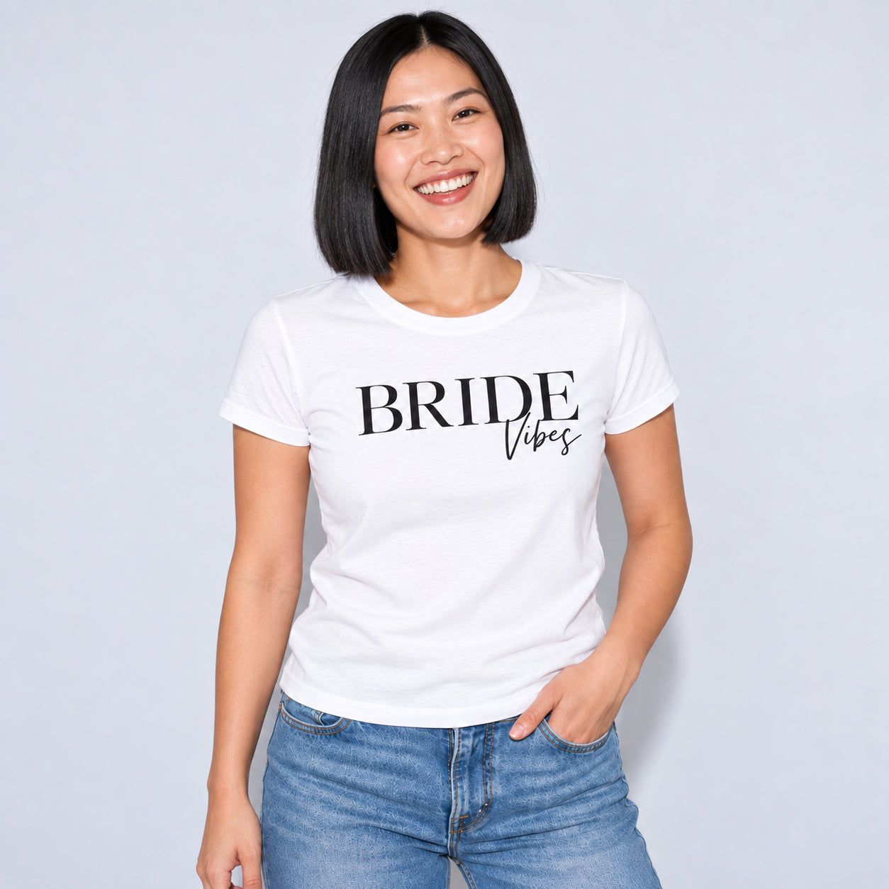 A woman with a short black bob hairstyle is wearing a white crewneck t-shirt with 'BRIDE vibes'.