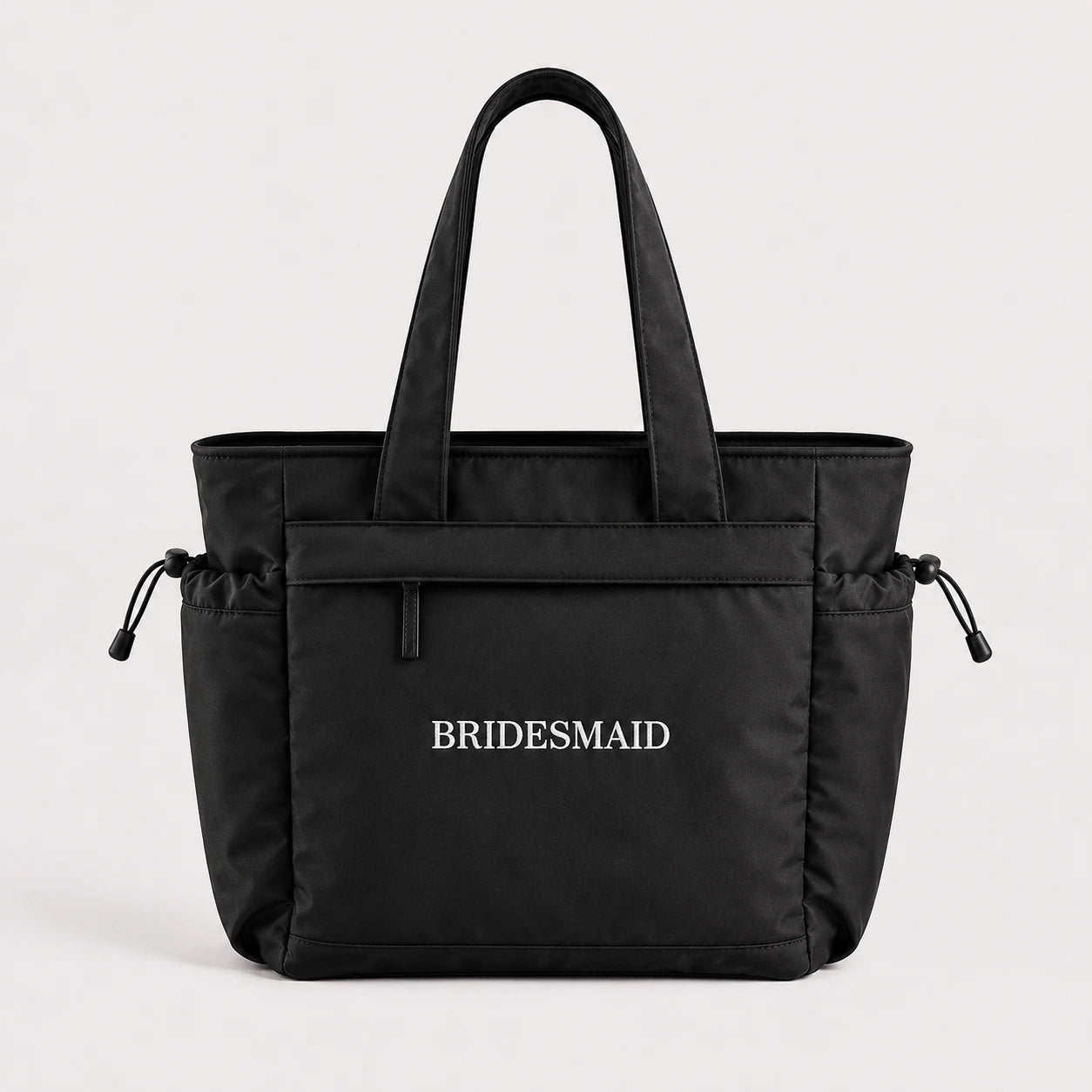 Black tote bag with 'BRIDESMAID' text on a light gray background