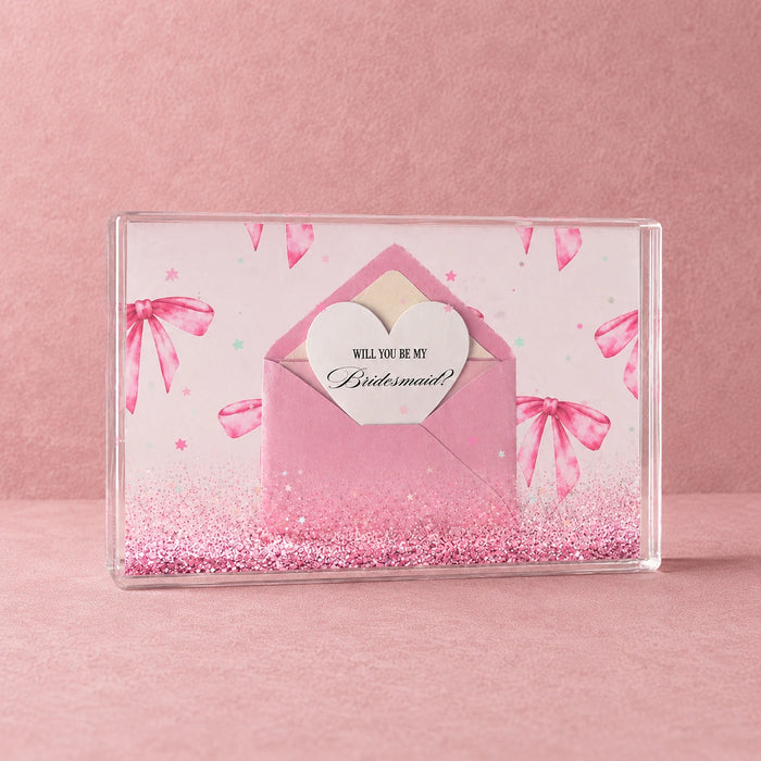 Bridesmaid proposal confetti block with pink envelope, heart card, glitter and star confetti on a textured pink background.