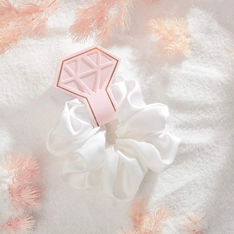 White scrunchie with pink geometric hair clip on a soft white background with pink decorative elements.