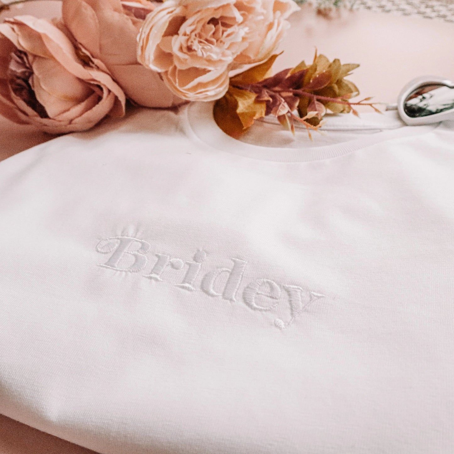 White t-shirt with 'Bridey' embroidery and peach roses on a white background