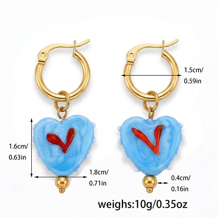 A pair of gold hoop earrings with light blue heart-shaped dangles featuring a red heart design in the center, shown with dimension lines and text indicating measurements and weight on a white background.