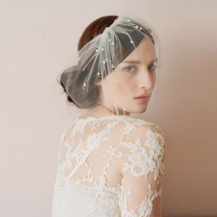 Woman wearing a lace wedding dress with a sheer headpiece against a plain background