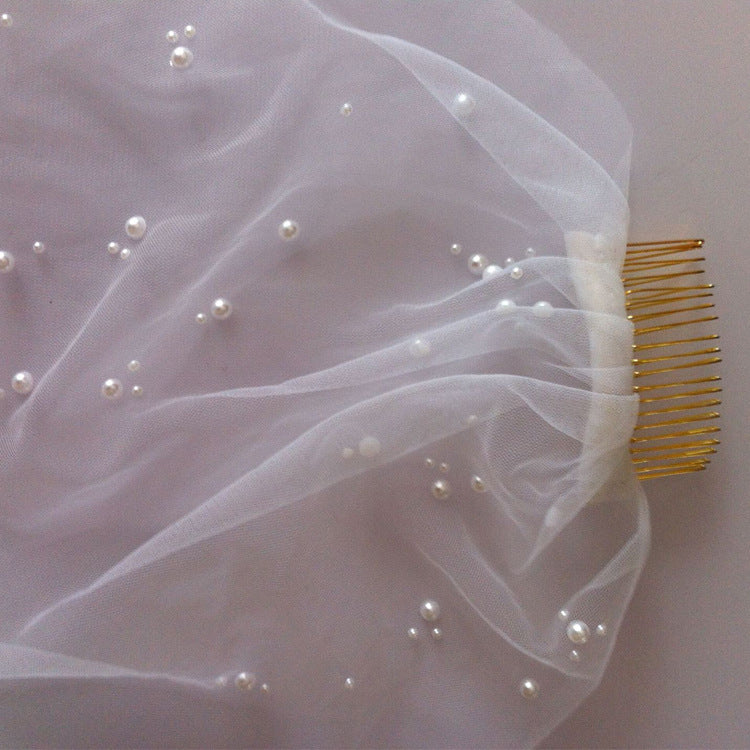White tulle bridal veil with scattered pearl beads and a gold comb hair accessory, shown on a neutral light background.