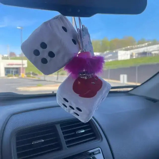 Pink feather disco ball car charm hanging from a rear view mirror with fuzzy dice inside a car.