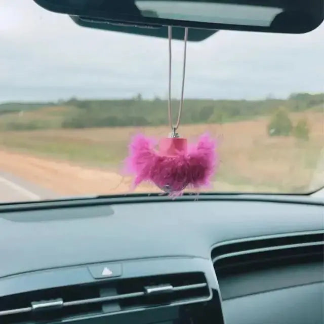 Pink feather disco ball car charm hanging from a rear view mirror inside a car.