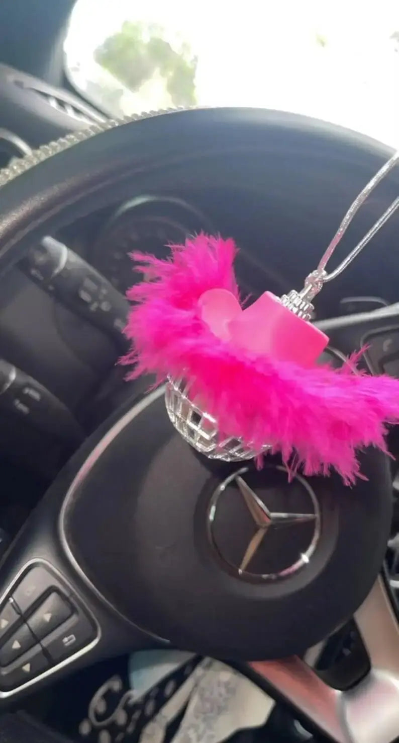 Pink feather disco ball car charm hanging inside a car above the steering wheel.