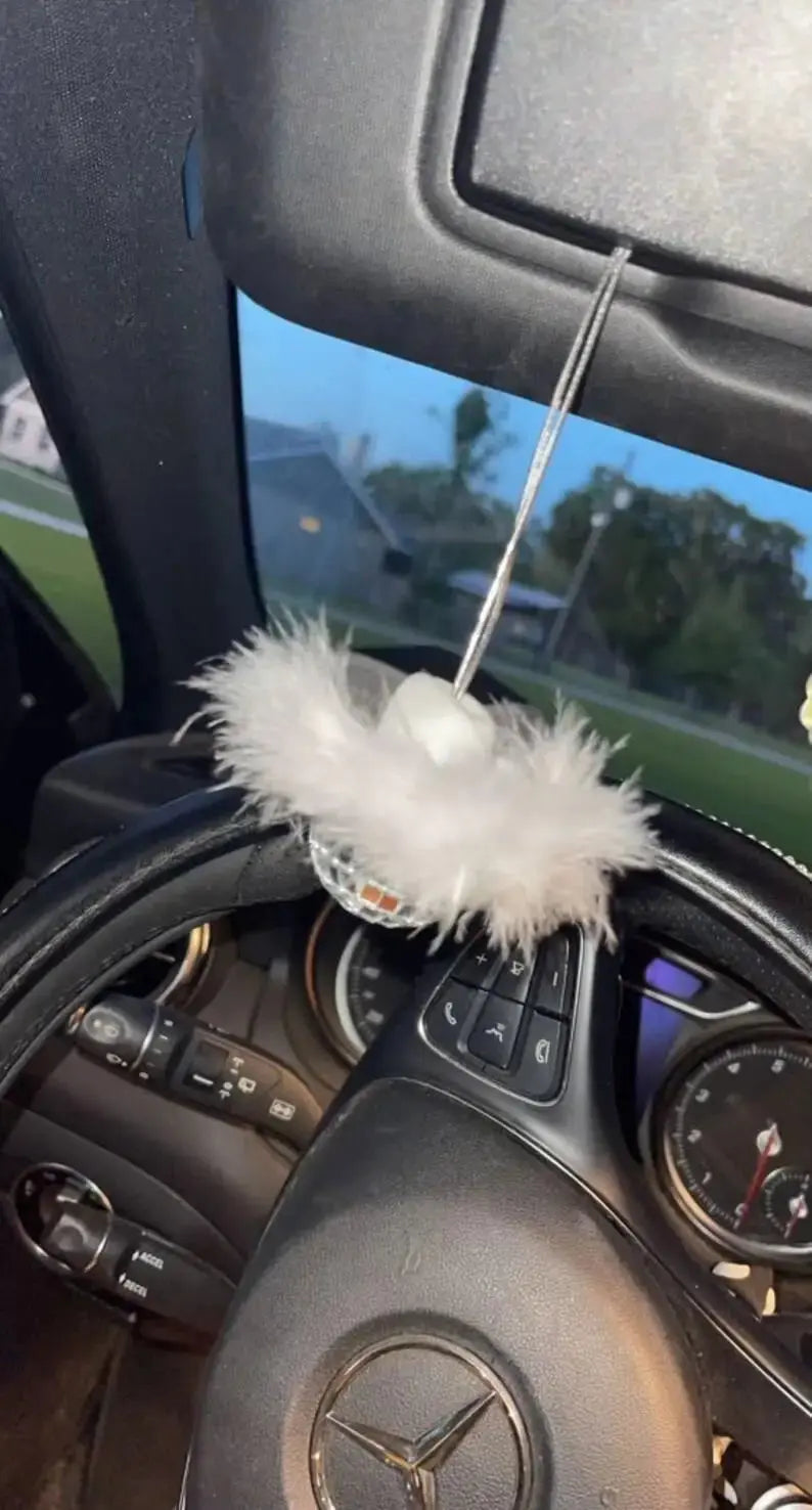 White feather disco ball car charm hanging inside a car above the steering wheel.