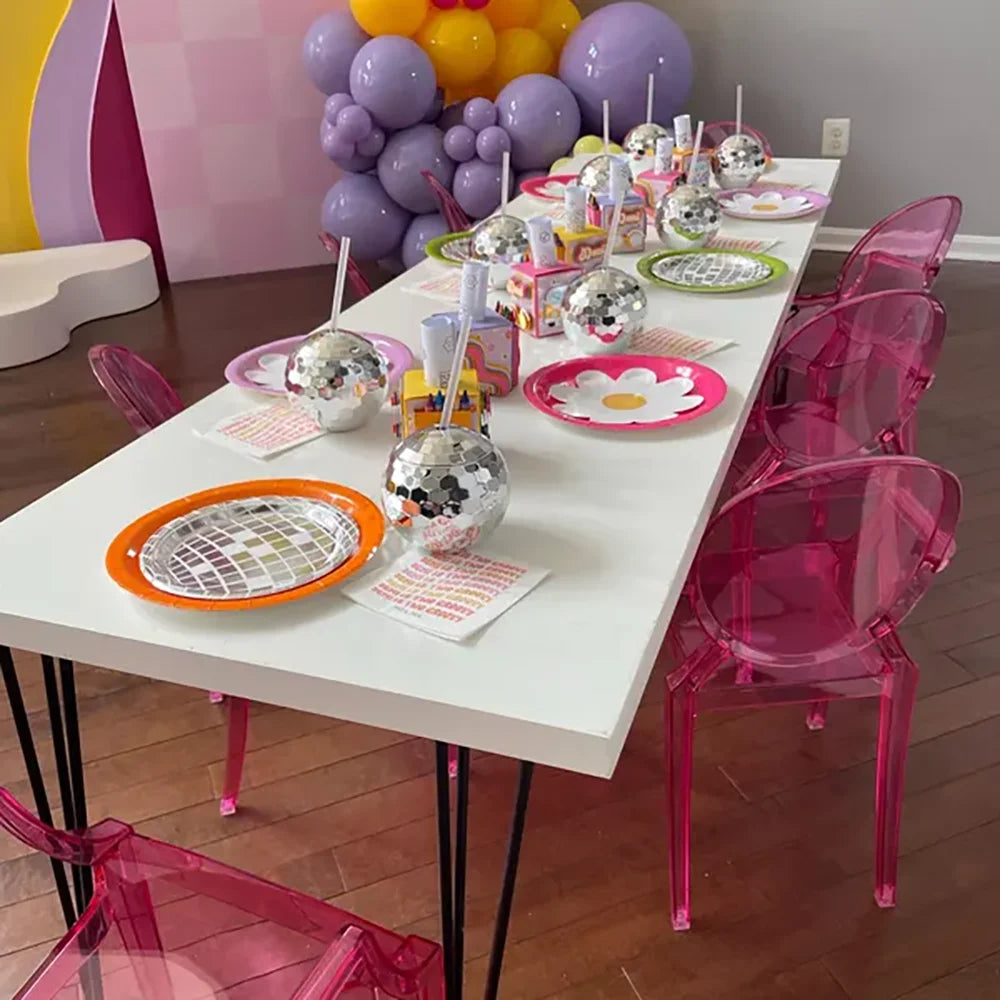 Decorated table with colorful balloons, disco cups, party supplies in a room with pink chairs.