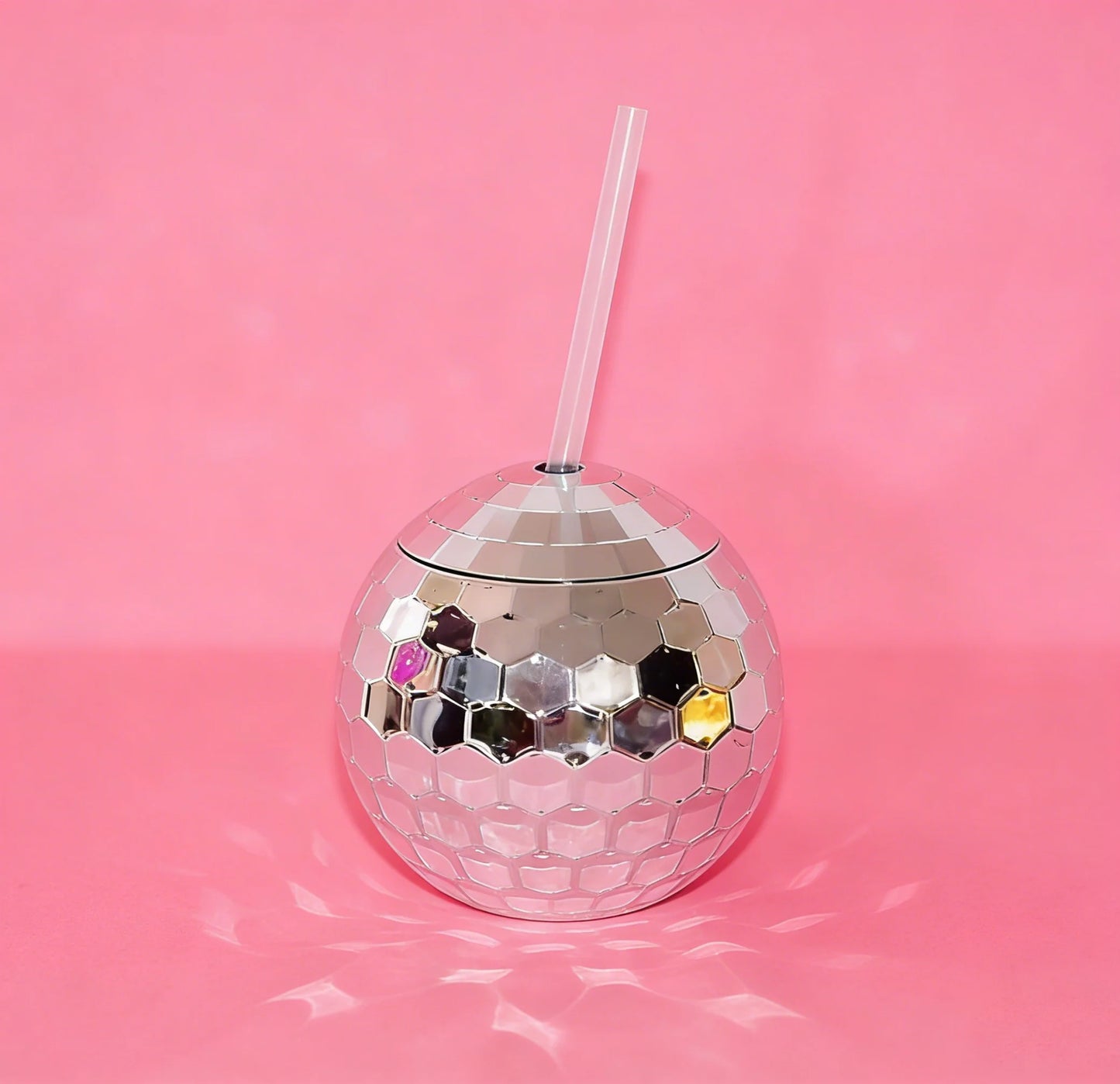 Silver disco ball tumbler with a straw on a pink background