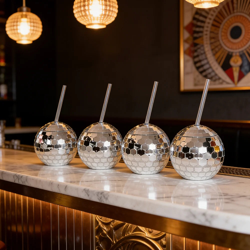 Four silver disco ball tumblers with straws on a marble bar counter.
