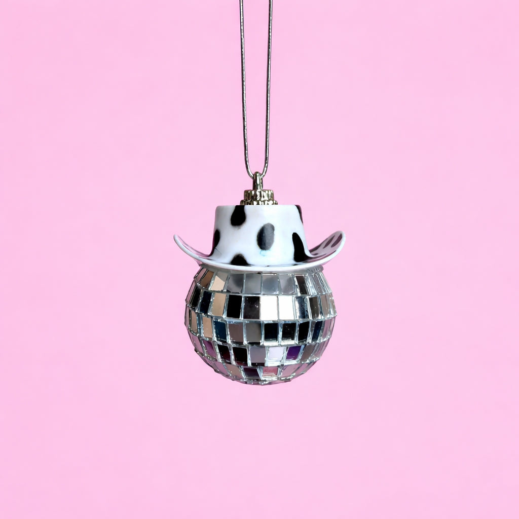 Black and white disco cowgirl car mirror charm with a cow print mini cowboy hat and mirrored disco ball on a soft pink background.