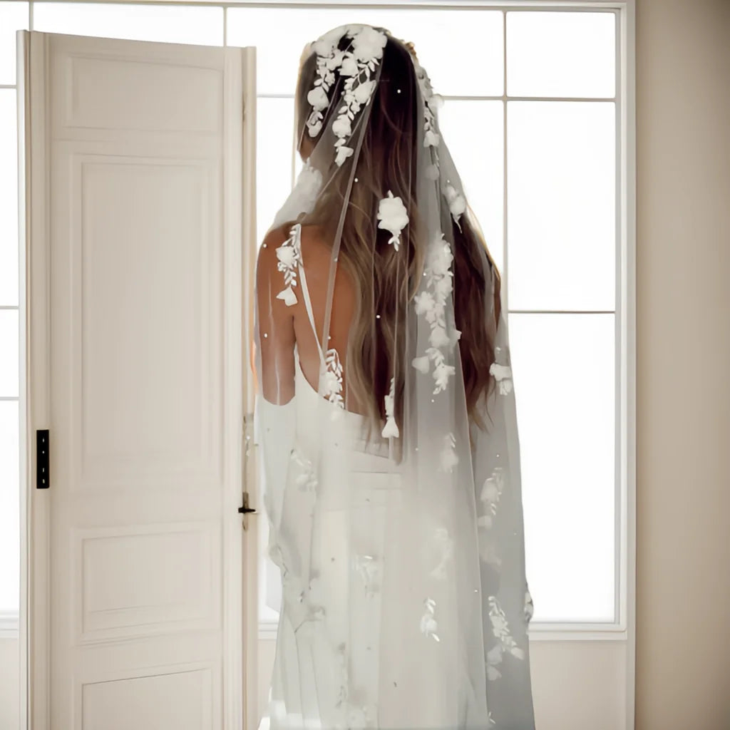 Back view of bride wearing a floral pearl bridal veil with soft tulle and flower appliqué near a doorway.
