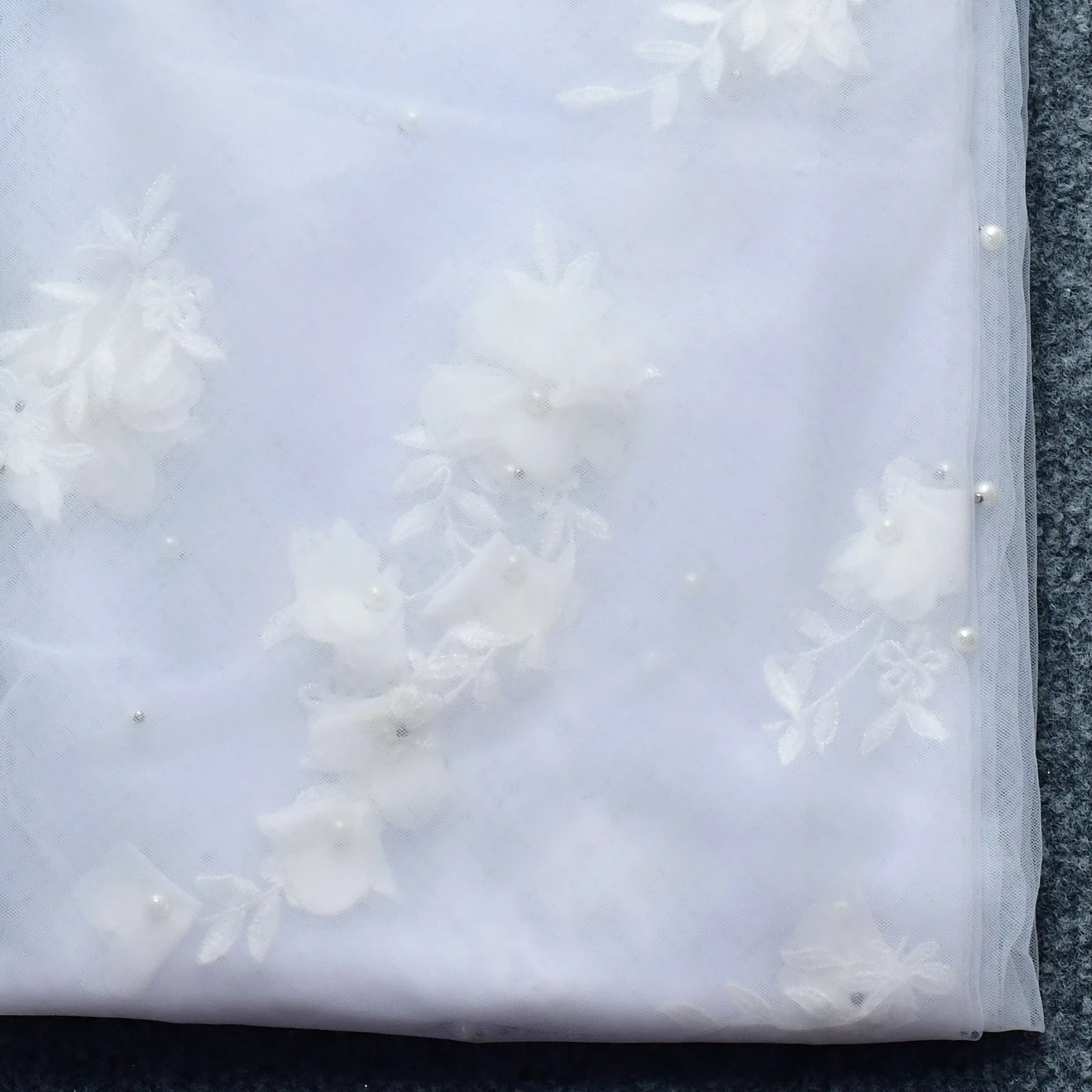 Close-up of floral appliqué and pearl-style beading on soft bridal veil tulle.