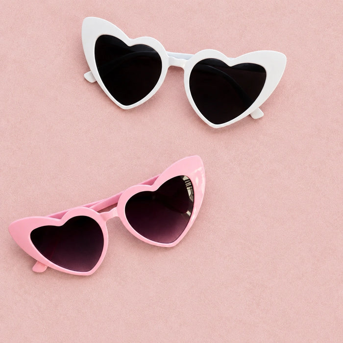 Heart-shaped sunglasses in white and pink on a pink background