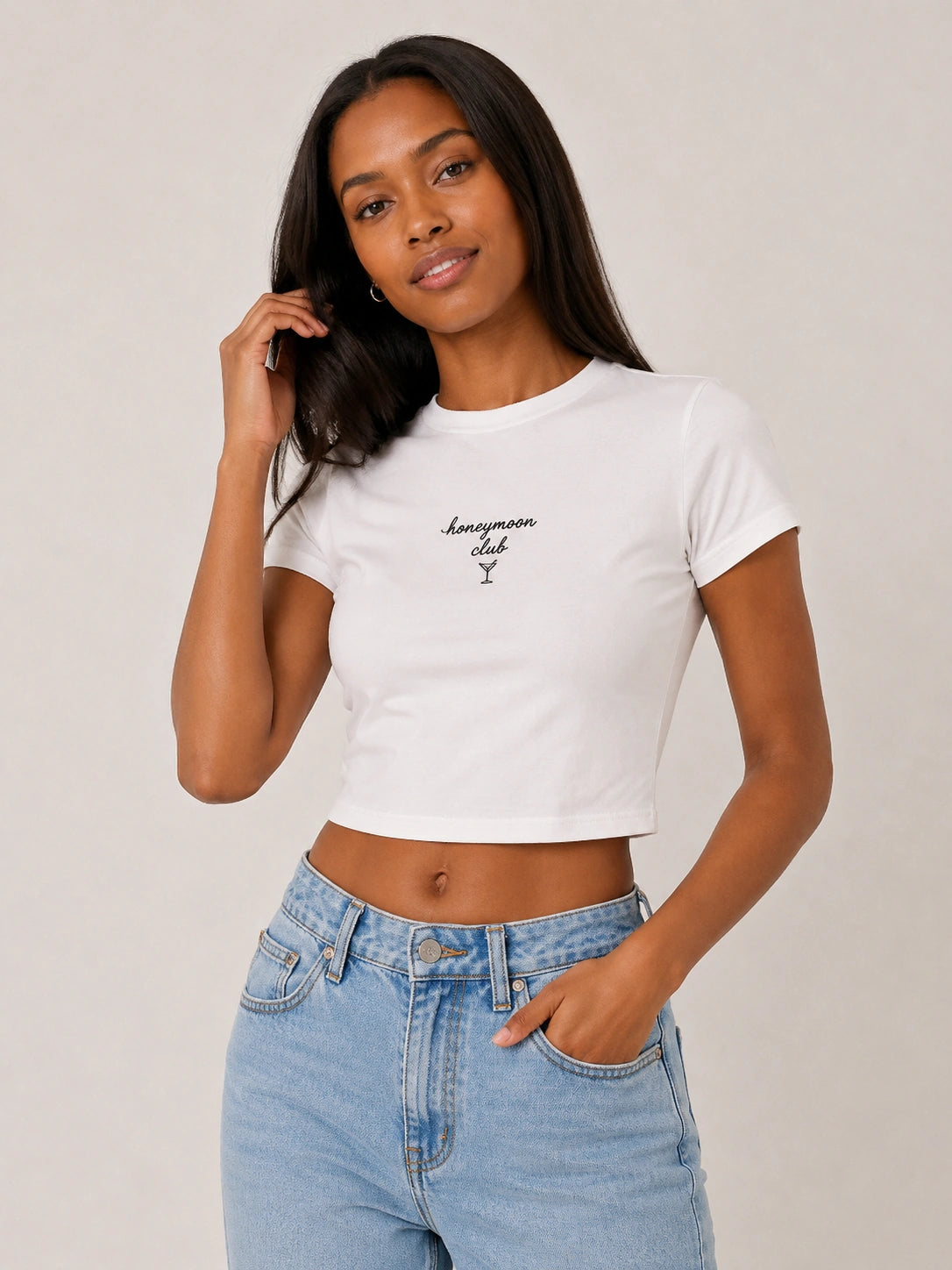 Woman wearing a white crop top with text and blue jeans on a plain background