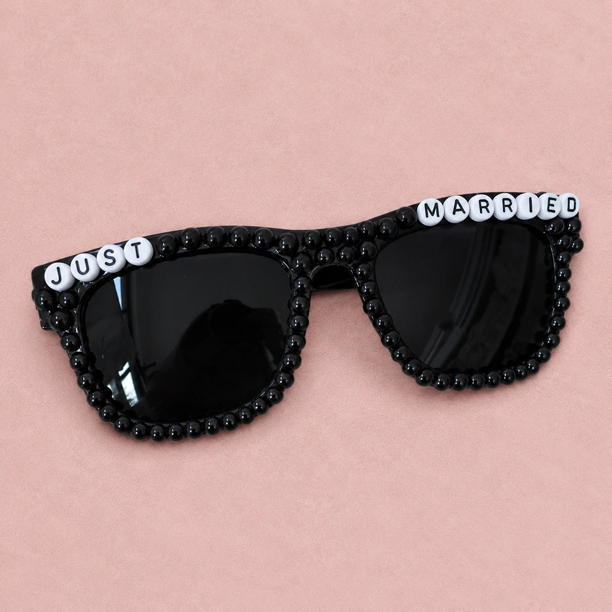 Black sunglasses with 'Just Married' text on a pink background